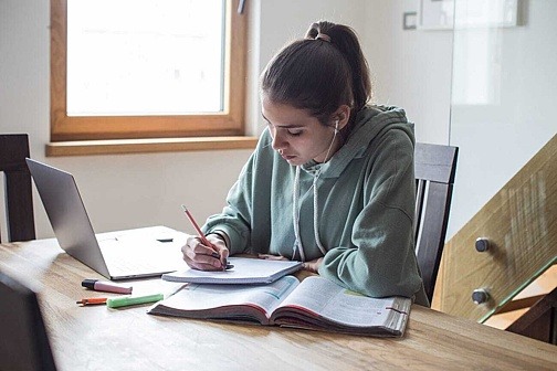 Schülerin arbeitet am Schreibtisch mit Laptop und Buch