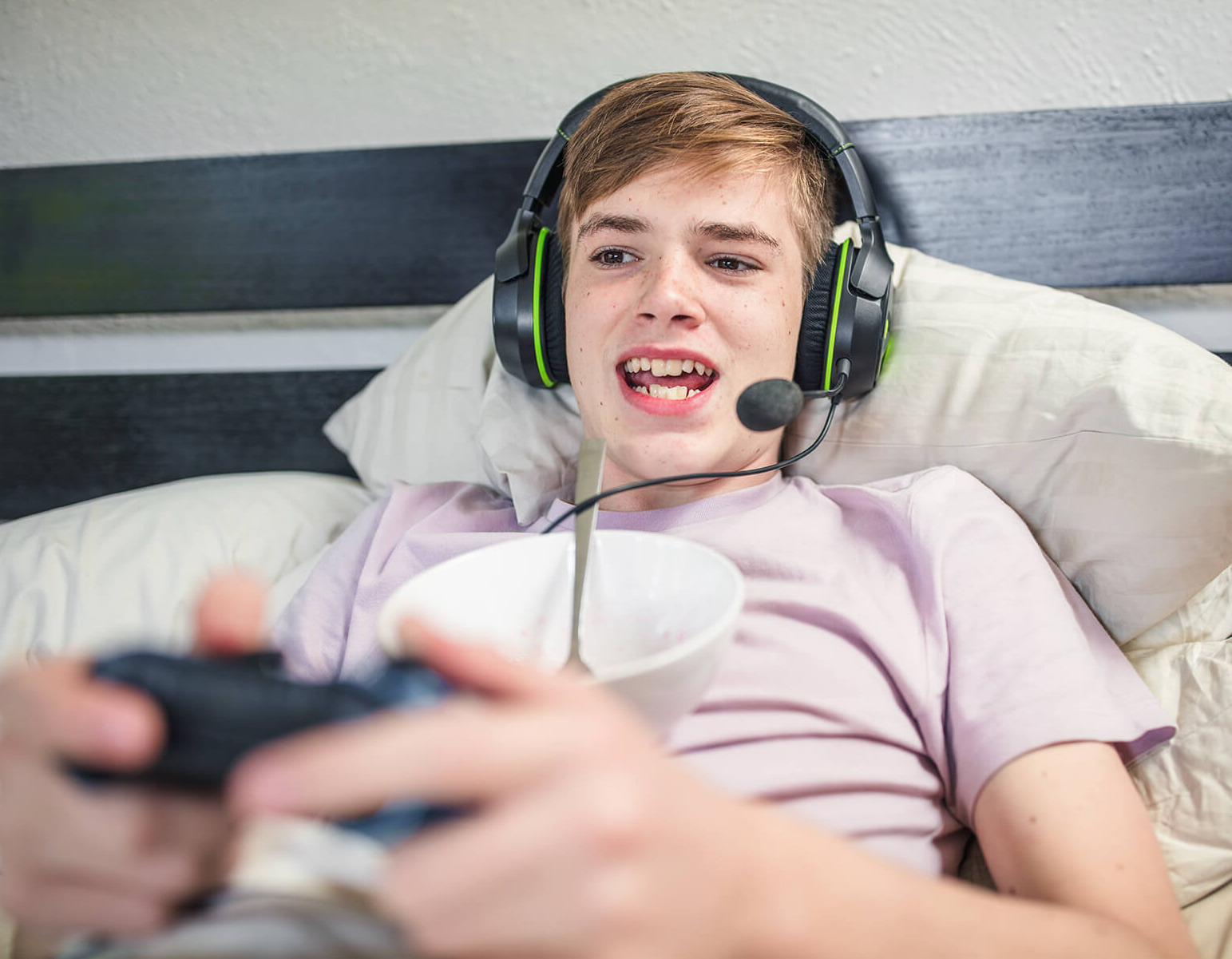 Junge liegt im Bett mit einem Headset und spielt ein Videospiel.