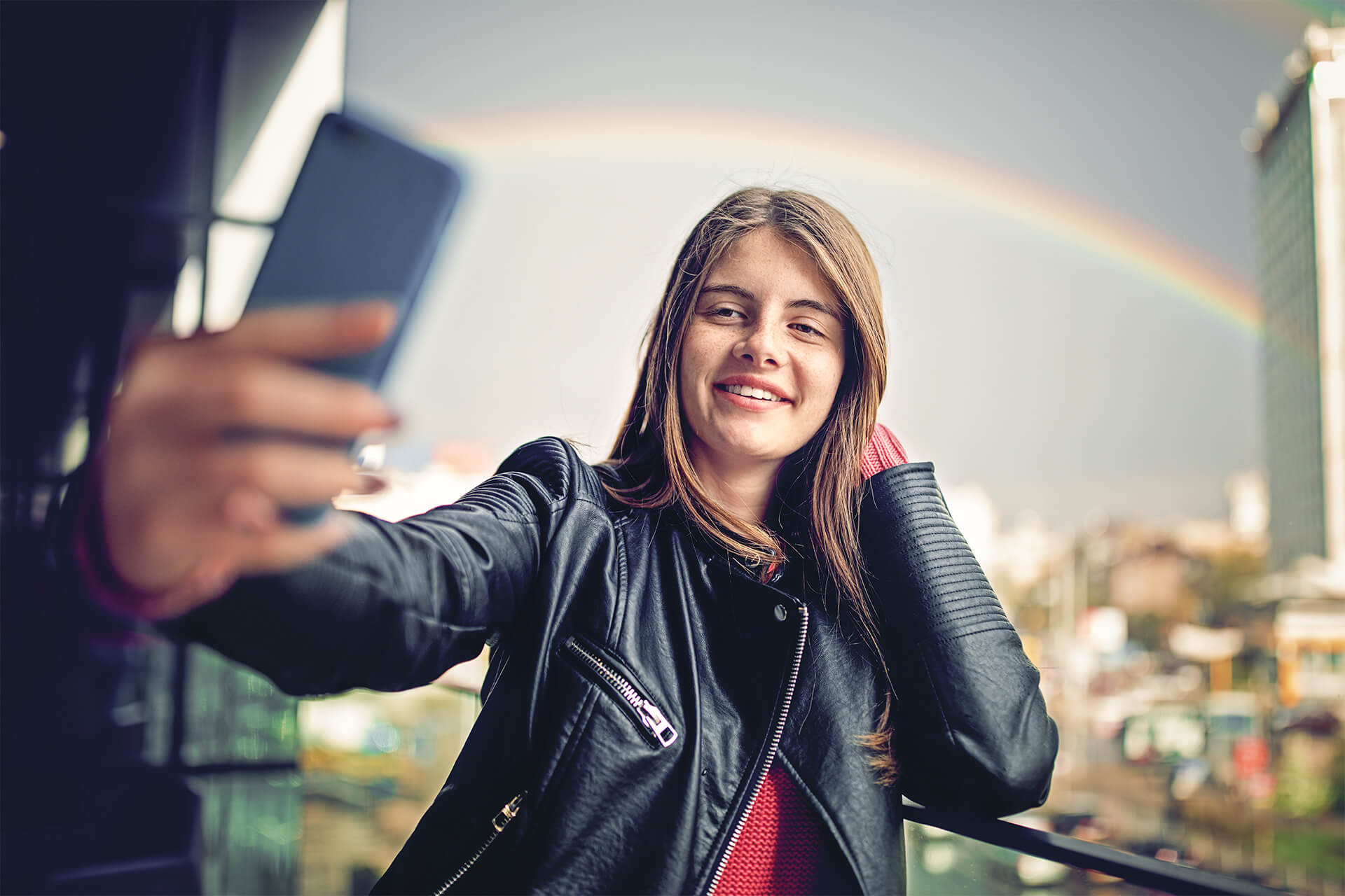 Mädchen macht ein Selfie. Im Hintergrund ist ein Regenbogen zu sehen.